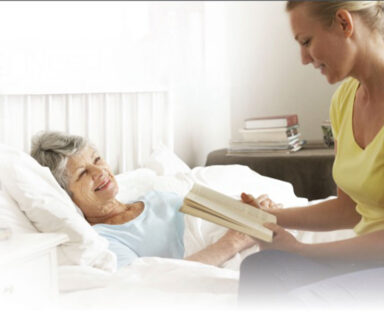 Caretaker reading to a cancer patient who is laying in bed